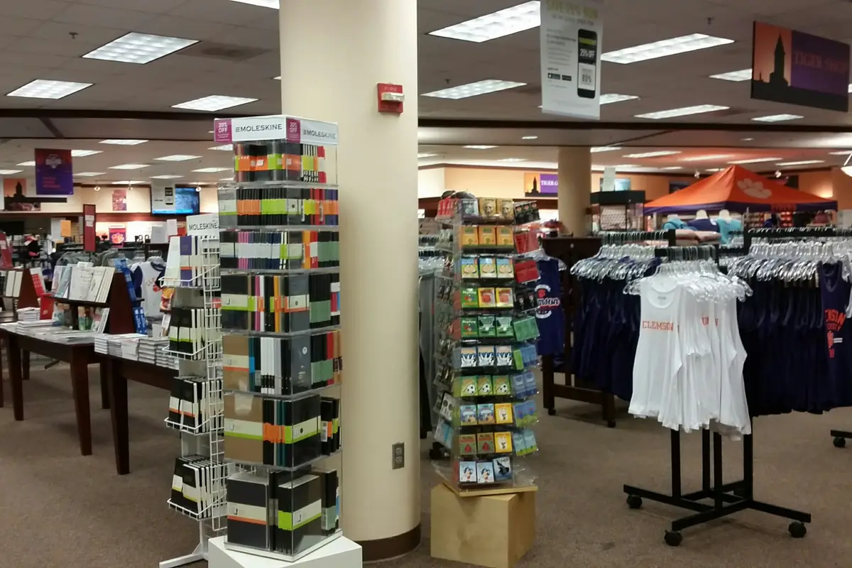 Inside a university bookstore: rails of branded clothing, display stands and tills under strip lights